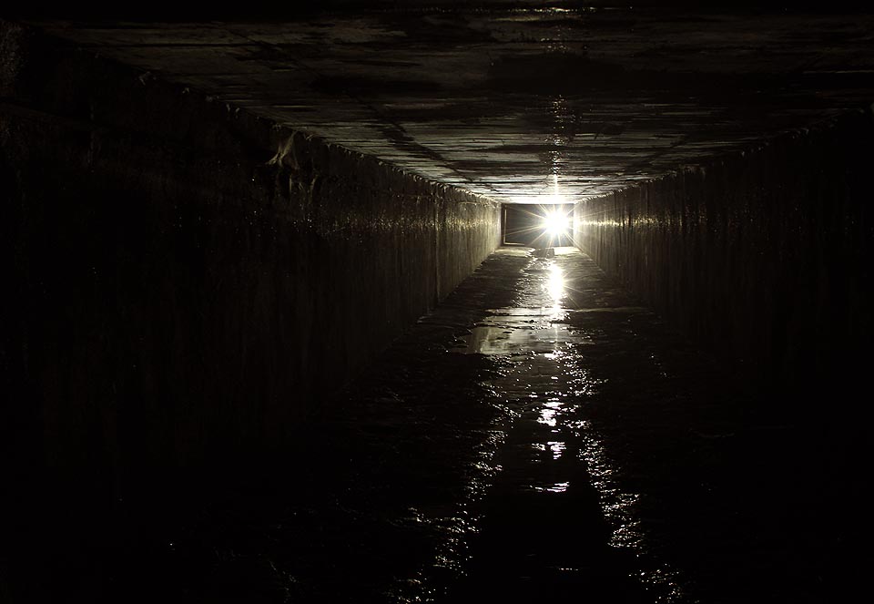 Tma je tu ve dne i v noci, i když na konci ještě prosvítá paprsek světla z posledního otvoru na povrch před Řípskou ulicí (za reflektorem vlevo).