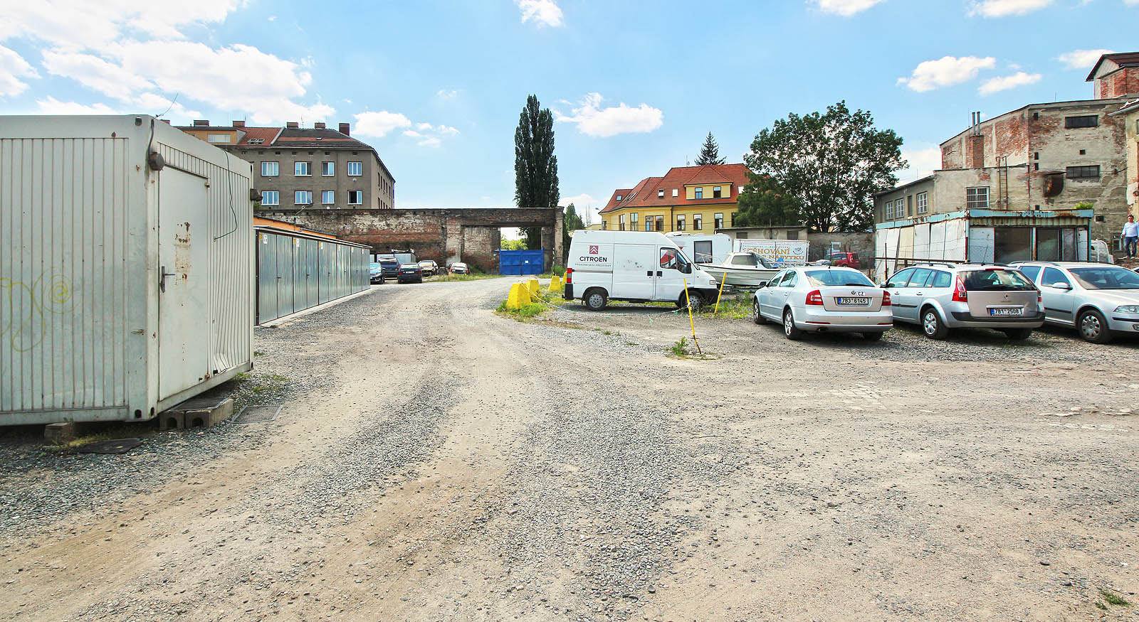 Tak vypadá skladový areál zevnitř. Vlečka do něj vcházela branou v pozadí a vedla z našeho pohledu vpravo rovnoběžně s uježděnou cestou, místem, kde stojí auta. Tak vypadá skladový areál zevnitř. Vlečka do něj vcházela branou v pozadí a vedla z našeho pohledu vpravo rovnoběžně s uježděnou cestou, místem, kde stojí auta.